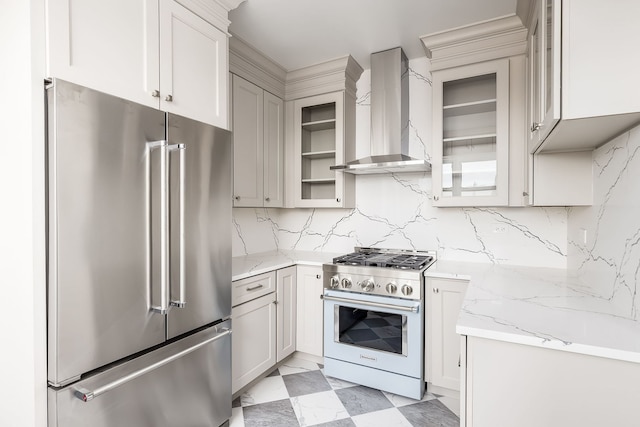 kitchen with white cabinetry, light stone countertops, wall chimney exhaust hood, tasteful backsplash, and high end appliances