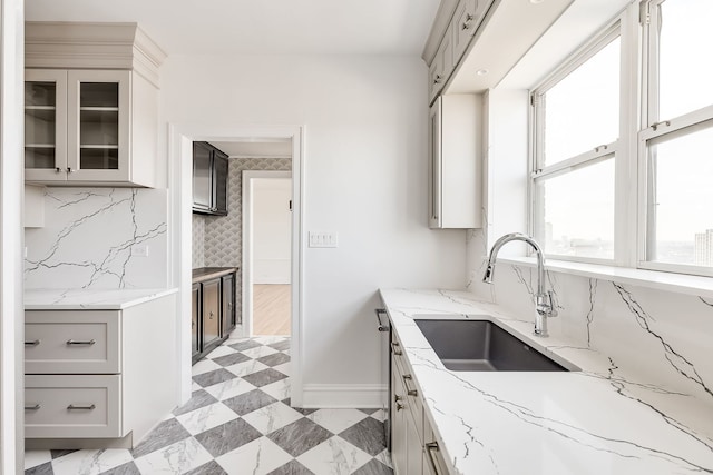 kitchen with gray cabinetry, backsplash, light stone counters, and sink