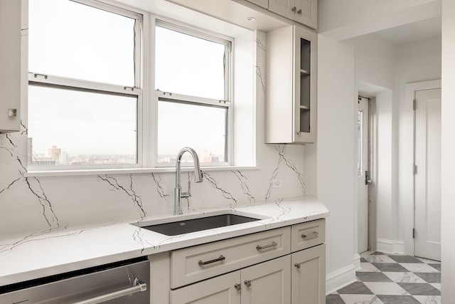 kitchen featuring tasteful backsplash, light stone counters, sink, and stainless steel dishwasher