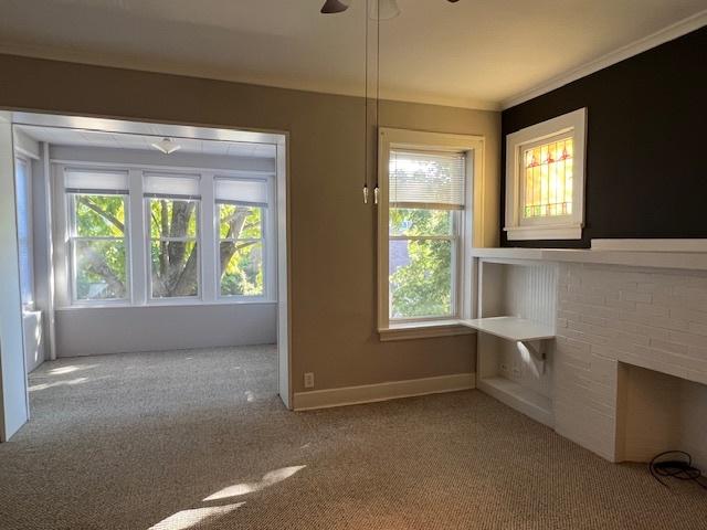 unfurnished living room featuring a wealth of natural light, light carpet, and ornamental molding