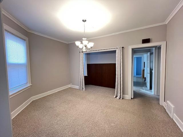 carpeted empty room with crown molding and a notable chandelier