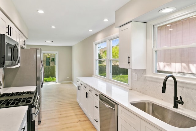 kitchen featuring appliances with stainless steel finishes, light wood-type flooring, backsplash, sink, and white cabinetry