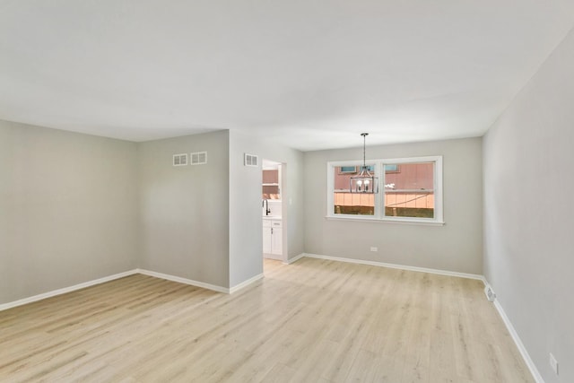 empty room with an inviting chandelier, light hardwood / wood-style flooring, and sink