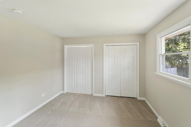 unfurnished bedroom featuring light colored carpet and two closets