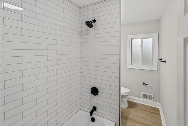 bathroom with hardwood / wood-style flooring, toilet, and tiled shower / bath