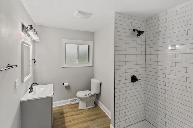 bathroom featuring a tile shower, hardwood / wood-style floors, vanity, and toilet