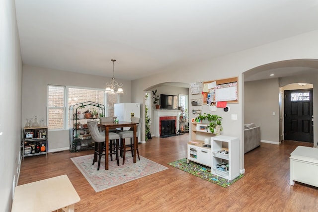 dining room with a brick fireplace, a wealth of natural light, hardwood / wood-style floors, and a notable chandelier