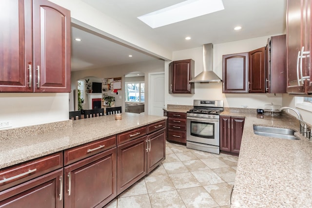 kitchen with light stone countertops, stainless steel gas stove, wall chimney exhaust hood, and sink