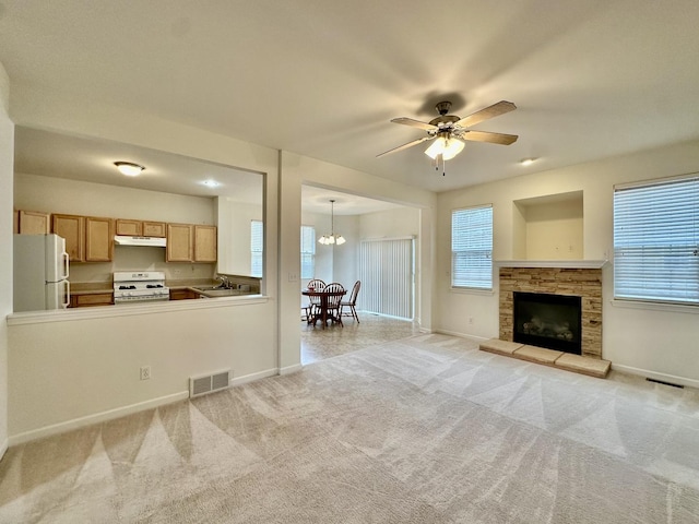 kitchen with white appliances, light colored carpet, ceiling fan with notable chandelier, a fireplace, and hanging light fixtures