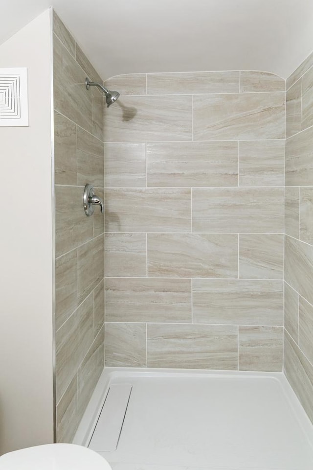 bathroom featuring tiled shower and toilet