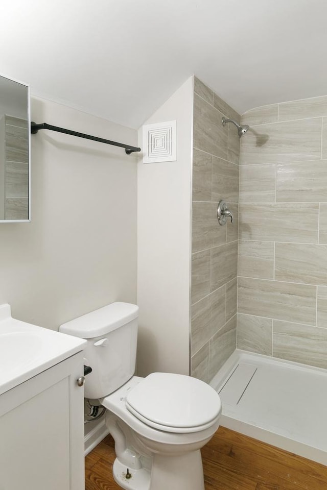 bathroom with a tile shower, vanity, wood-type flooring, and toilet