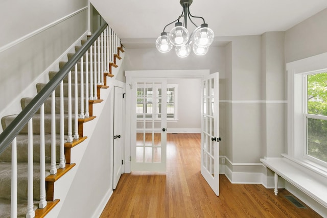 stairway featuring a chandelier, wood-type flooring, french doors, and plenty of natural light