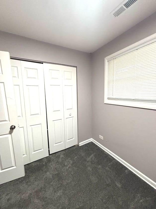 unfurnished bedroom with dark colored carpet and a closet