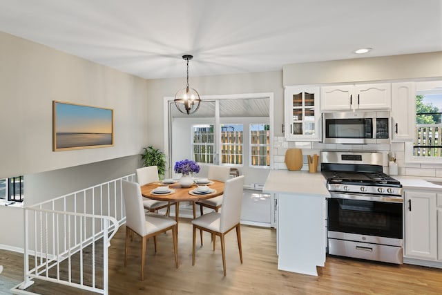 kitchen with pendant lighting, appliances with stainless steel finishes, tasteful backsplash, a notable chandelier, and white cabinetry