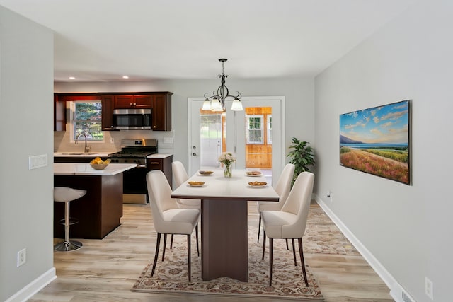 dining room with light wood-type flooring, sink, and an inviting chandelier