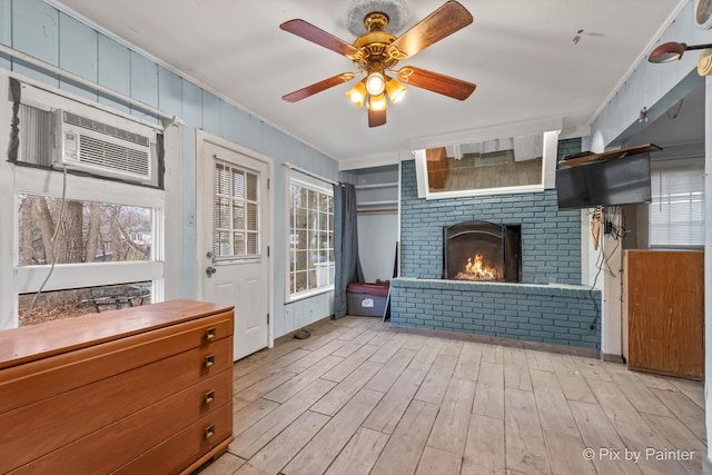 interior space featuring a wall mounted air conditioner, light wood-type flooring, a brick fireplace, ceiling fan, and crown molding