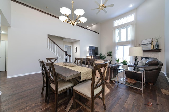 dining area featuring ceiling fan with notable chandelier, dark hardwood / wood-style floors, a high ceiling, and a wealth of natural light