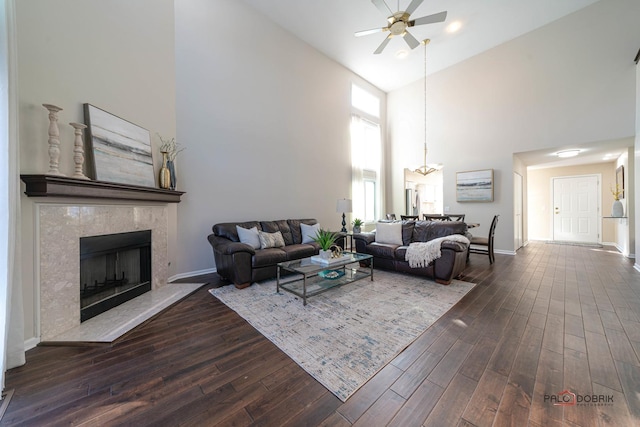 living room featuring dark wood-type flooring, a premium fireplace, and ceiling fan with notable chandelier