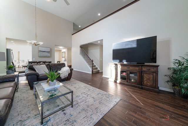 living room with a towering ceiling, dark hardwood / wood-style flooring, and ceiling fan with notable chandelier