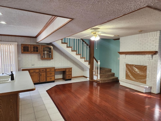 interior space with ceiling fan, a brick fireplace, crown molding, a textured ceiling, and light tile patterned floors