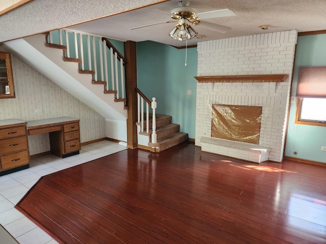 unfurnished living room with a textured ceiling, light hardwood / wood-style floors, a brick fireplace, and ceiling fan