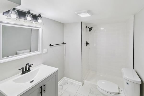 bathroom with tiled shower, vanity, and toilet