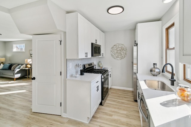 kitchen featuring white cabinets, sink, light hardwood / wood-style flooring, decorative backsplash, and stainless steel appliances