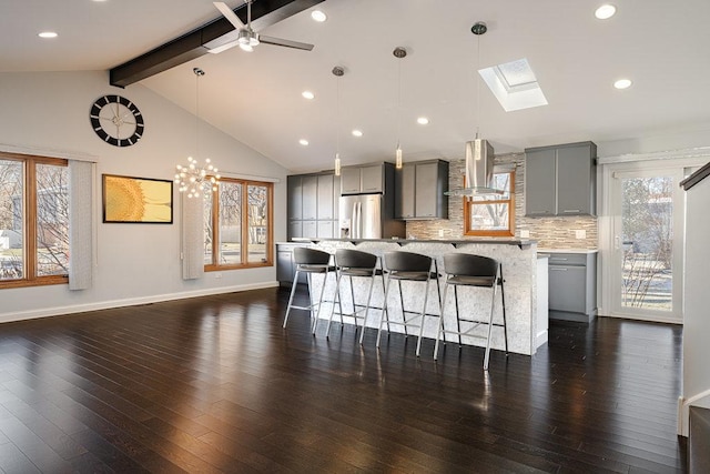 kitchen with backsplash, stainless steel refrigerator with ice dispenser, wall chimney exhaust hood, gray cabinets, and a kitchen island