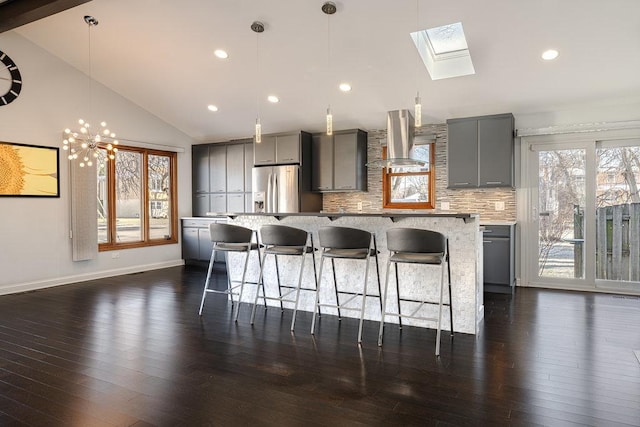 kitchen featuring gray cabinetry, a kitchen island, stainless steel refrigerator with ice dispenser, and ventilation hood