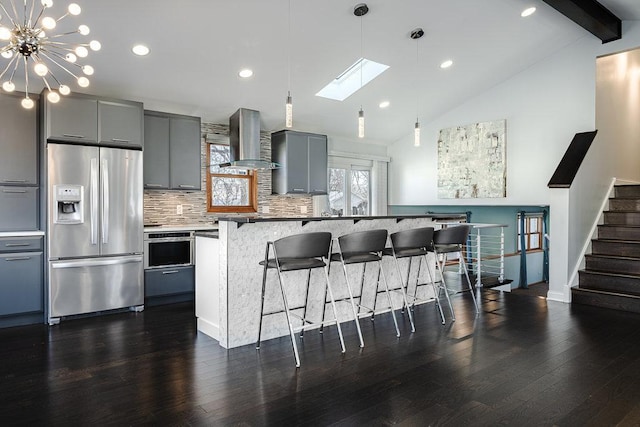 kitchen featuring a center island, backsplash, wall chimney range hood, gray cabinets, and stainless steel appliances