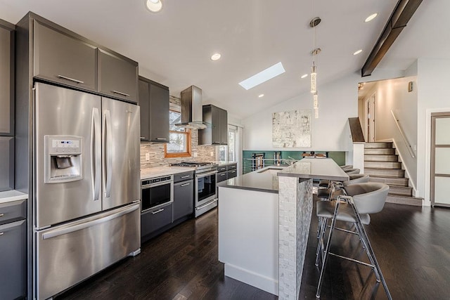 kitchen with a kitchen bar, backsplash, wall chimney exhaust hood, vaulted ceiling with skylight, and stainless steel appliances