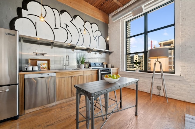 kitchen featuring wooden ceiling, sink, appliances with stainless steel finishes, light hardwood / wood-style floors, and brick wall