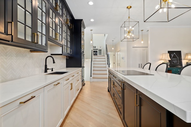 kitchen featuring black electric stovetop, sink, a notable chandelier, white cabinets, and hanging light fixtures