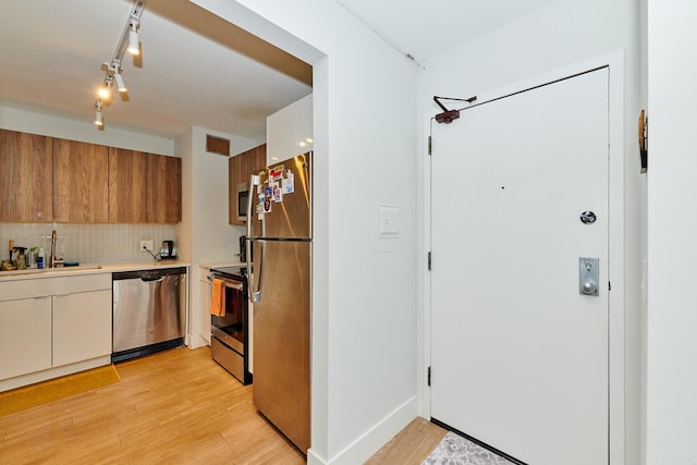 kitchen with light wood-type flooring, backsplash, stainless steel appliances, sink, and white cabinetry