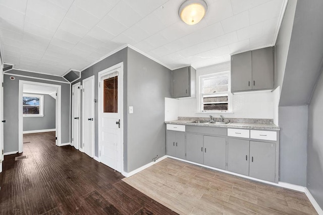 kitchen with gray cabinetry, crown molding, sink, and wood-type flooring