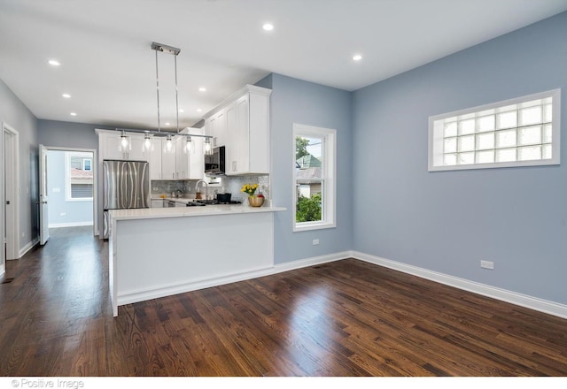 kitchen featuring white cabinetry, dark wood-type flooring, kitchen peninsula, stainless steel fridge, and pendant lighting