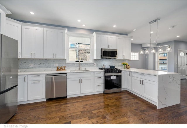 kitchen featuring kitchen peninsula, stainless steel appliances, sink, decorative light fixtures, and white cabinets