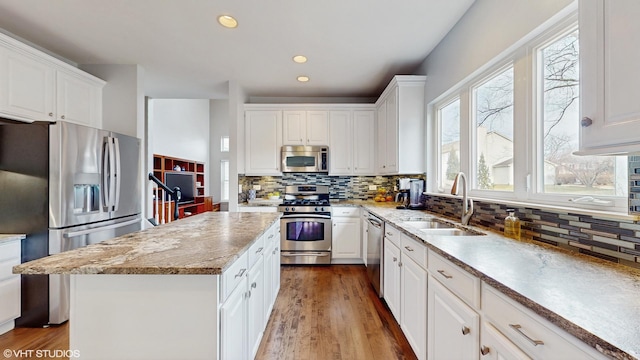 kitchen featuring white cabinetry, sink, stainless steel appliances, light hardwood / wood-style flooring, and a kitchen island