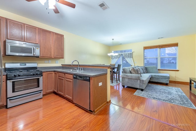 kitchen featuring kitchen peninsula, appliances with stainless steel finishes, light wood-type flooring, sink, and pendant lighting