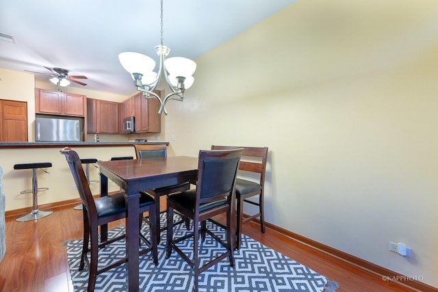 dining area with dark hardwood / wood-style flooring and ceiling fan with notable chandelier