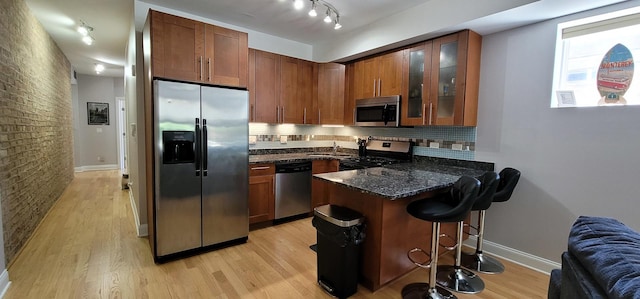 kitchen featuring stainless steel appliances, dark stone countertops, light hardwood / wood-style floors, decorative backsplash, and a breakfast bar