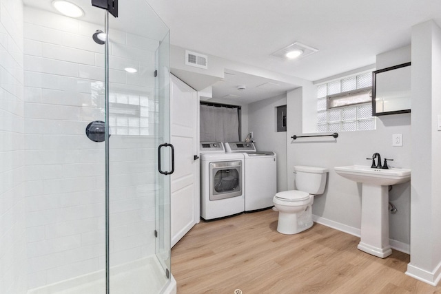 bathroom with a shower with shower door, toilet, wood-type flooring, and washing machine and clothes dryer