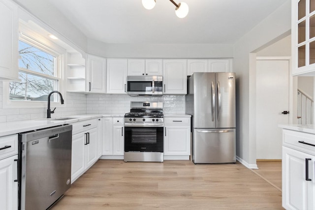 kitchen with white cabinets, sink, light hardwood / wood-style flooring, light stone countertops, and appliances with stainless steel finishes