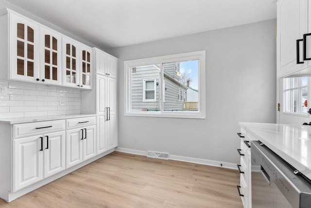 kitchen featuring tasteful backsplash, stainless steel dishwasher, white cabinets, light hardwood / wood-style floors, and plenty of natural light