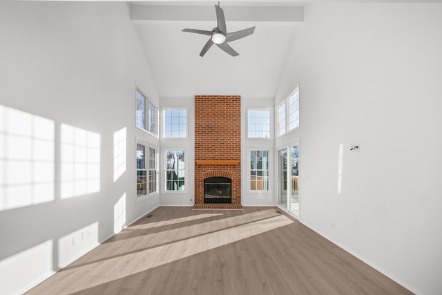 unfurnished living room with beamed ceiling, a brick fireplace, light hardwood / wood-style flooring, and high vaulted ceiling