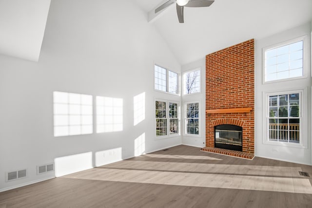 unfurnished living room with hardwood / wood-style flooring, ceiling fan, a towering ceiling, and a fireplace