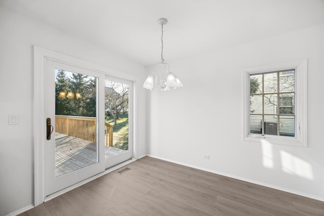 unfurnished dining area with hardwood / wood-style flooring, a wealth of natural light, and an inviting chandelier