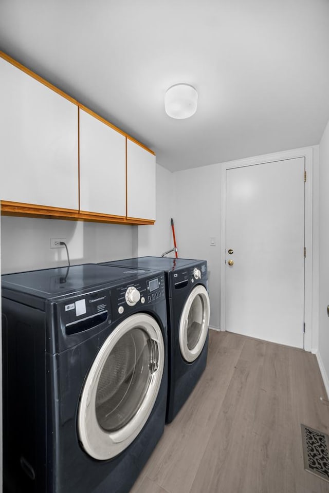 clothes washing area featuring cabinets, light hardwood / wood-style floors, and washing machine and clothes dryer