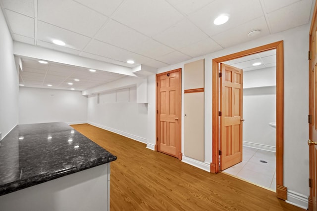 interior space featuring dark stone countertops, white cabinetry, light hardwood / wood-style flooring, and a drop ceiling