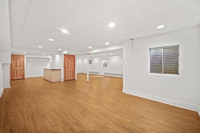 unfurnished living room with light hardwood / wood-style floors, a drop ceiling, and a baseboard heating unit